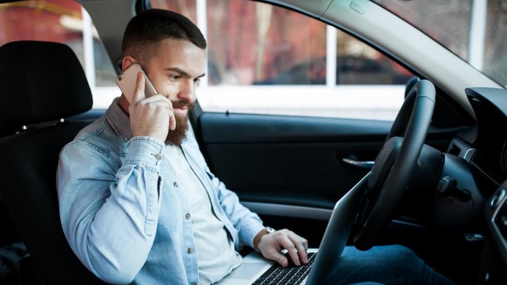 ZZP’er bespreekt leaseoptie vanuit auto terwijl hij werkt op laptop en belt – shortlease ZZP als flexibele keuze